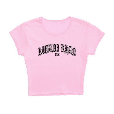 A light pink cropped t-shirt by Kublai Khan TX, featuring bold black Gothic lettering on the front. This presale item ships starting 10/17/25.