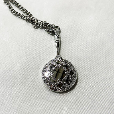 The PVRIS silver pendant necklace features a circular, ornate filigree design with a raised intricate pattern and shiny finish, displayed on a white textured surface.