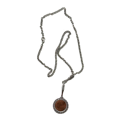 A PVRIS silver chain necklace features a circular brown pendant bordered by decorative silver, creating an elegant jewelry piece displayed on a white background.