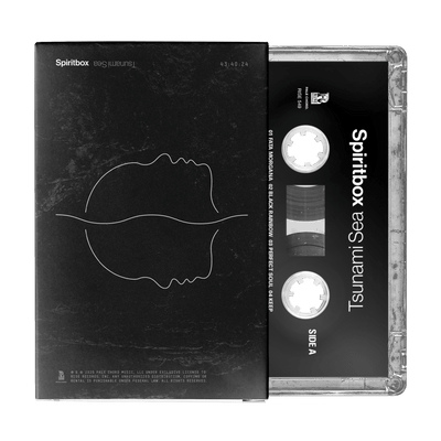 A Spiritbox black liner cassette tape for “Tsunami Sea” partially slides from its case, which shows minimalist white line art of two mirrored faces on a dark background; the tape itself displays the album title and side label.